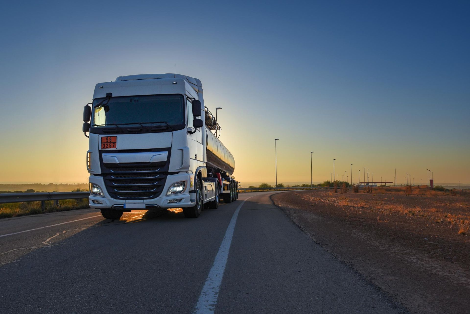 A white semi truck is driving down a highway at sunset.