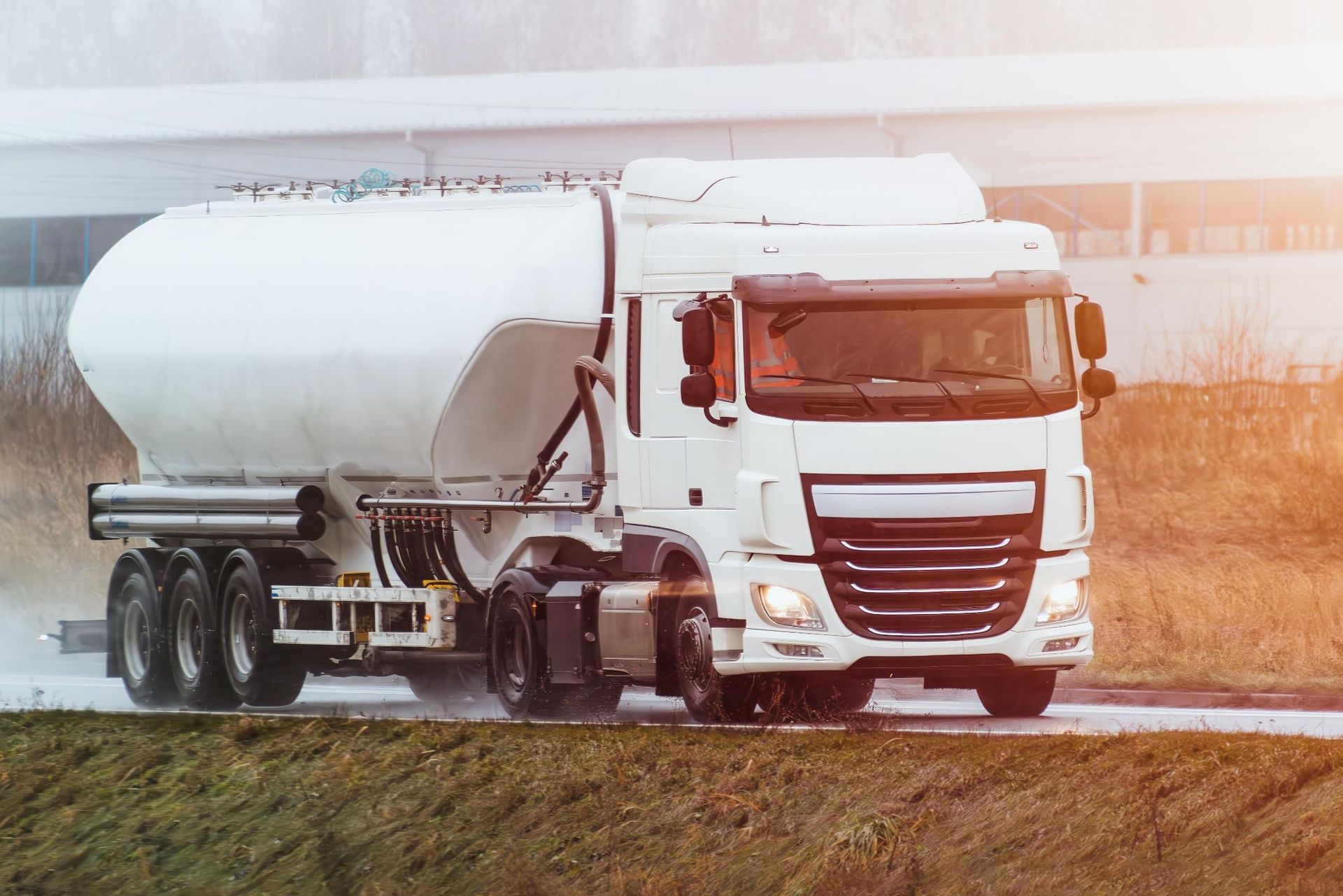 A white semi truck is driving down a wet road.