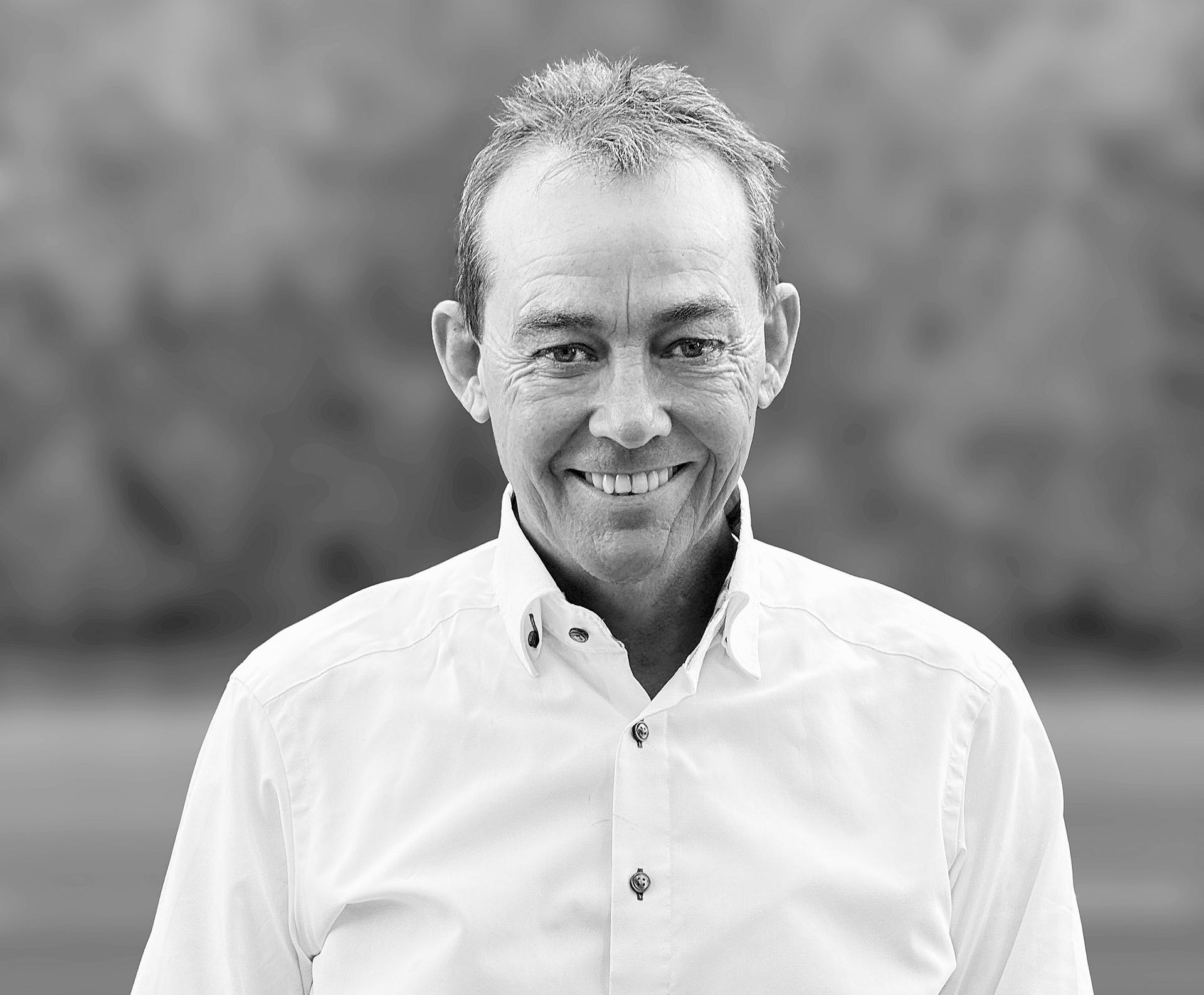 Auf einem Schwarzweißfoto lächelt ein Mann im weißen Hemd.