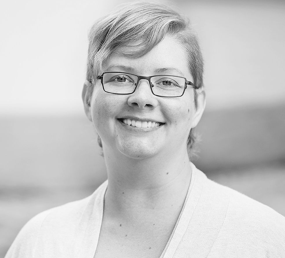 Eine Frau mit Brille lächelt auf einem Schwarzweißfoto.