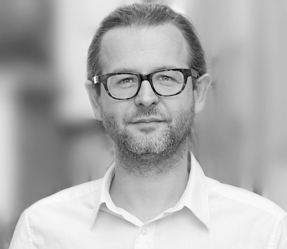 Ein Schwarzweißfoto eines Mannes mit Brille und weißem Hemd.