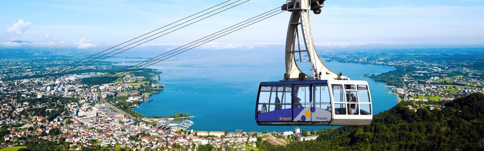Eine Seilbahn fliegt über einen See mit einer Stadt im Hintergrund.