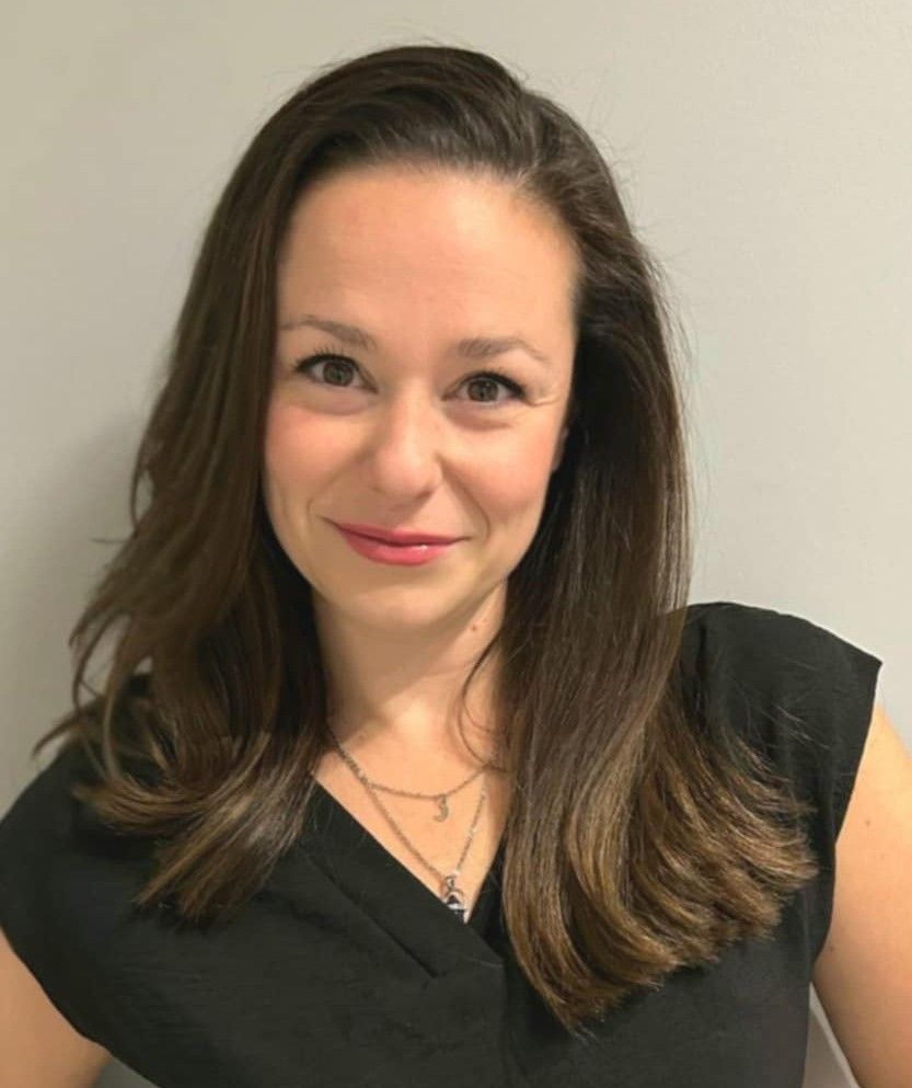 Woman with brown hair smiles, wearing a black top and layered necklace.