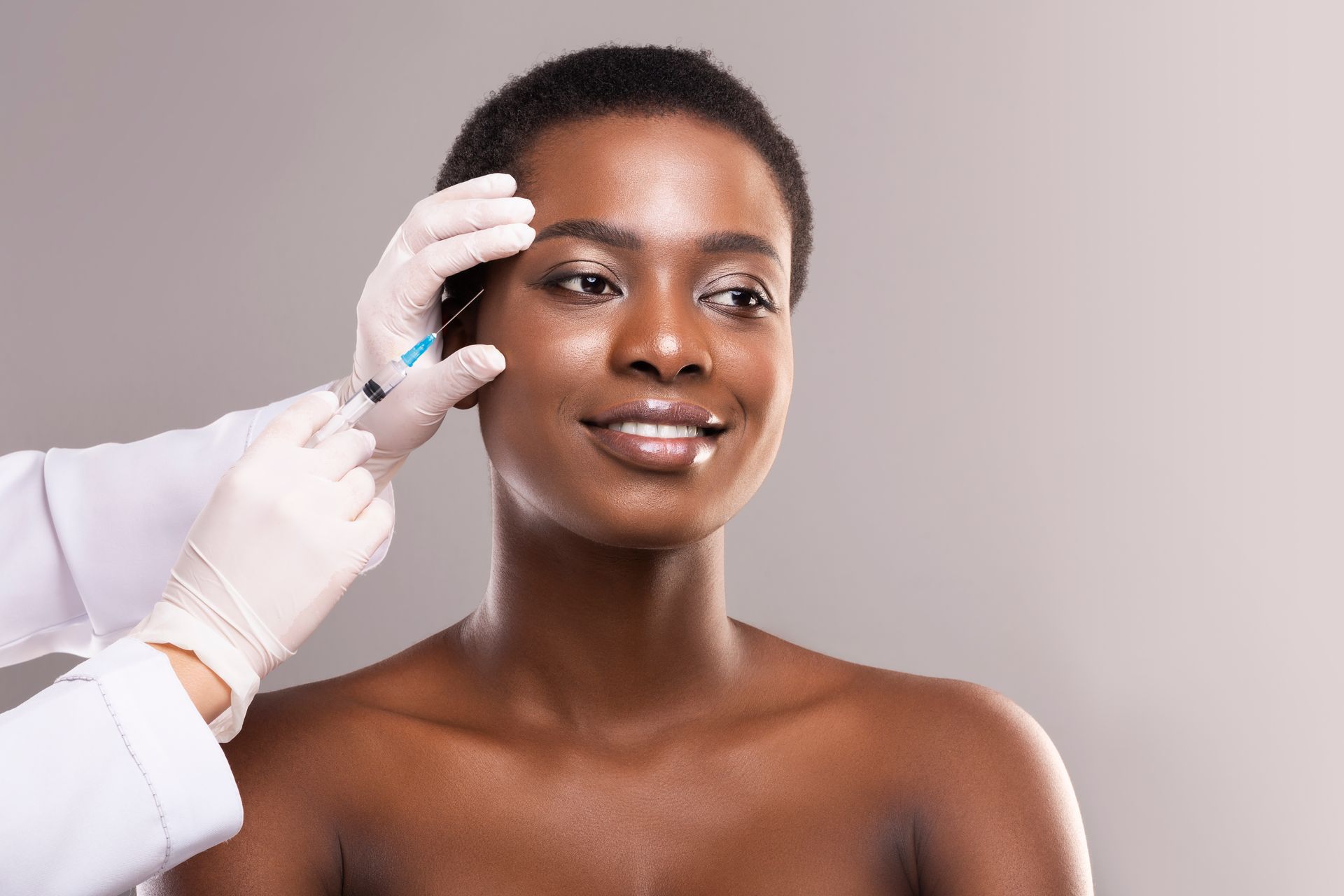 Person receiving a facial treatment while a gloved hand applies cream to the forehead