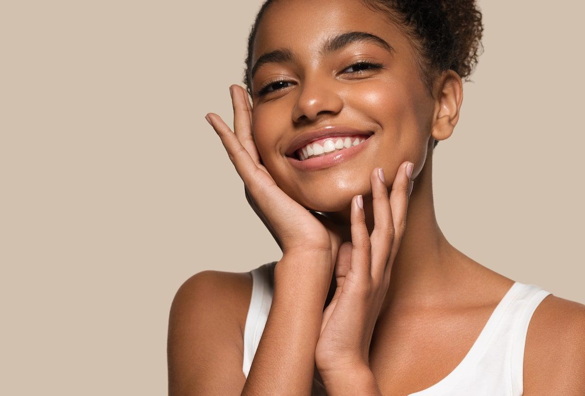 Smiling person gently touching their face against a beige background.
