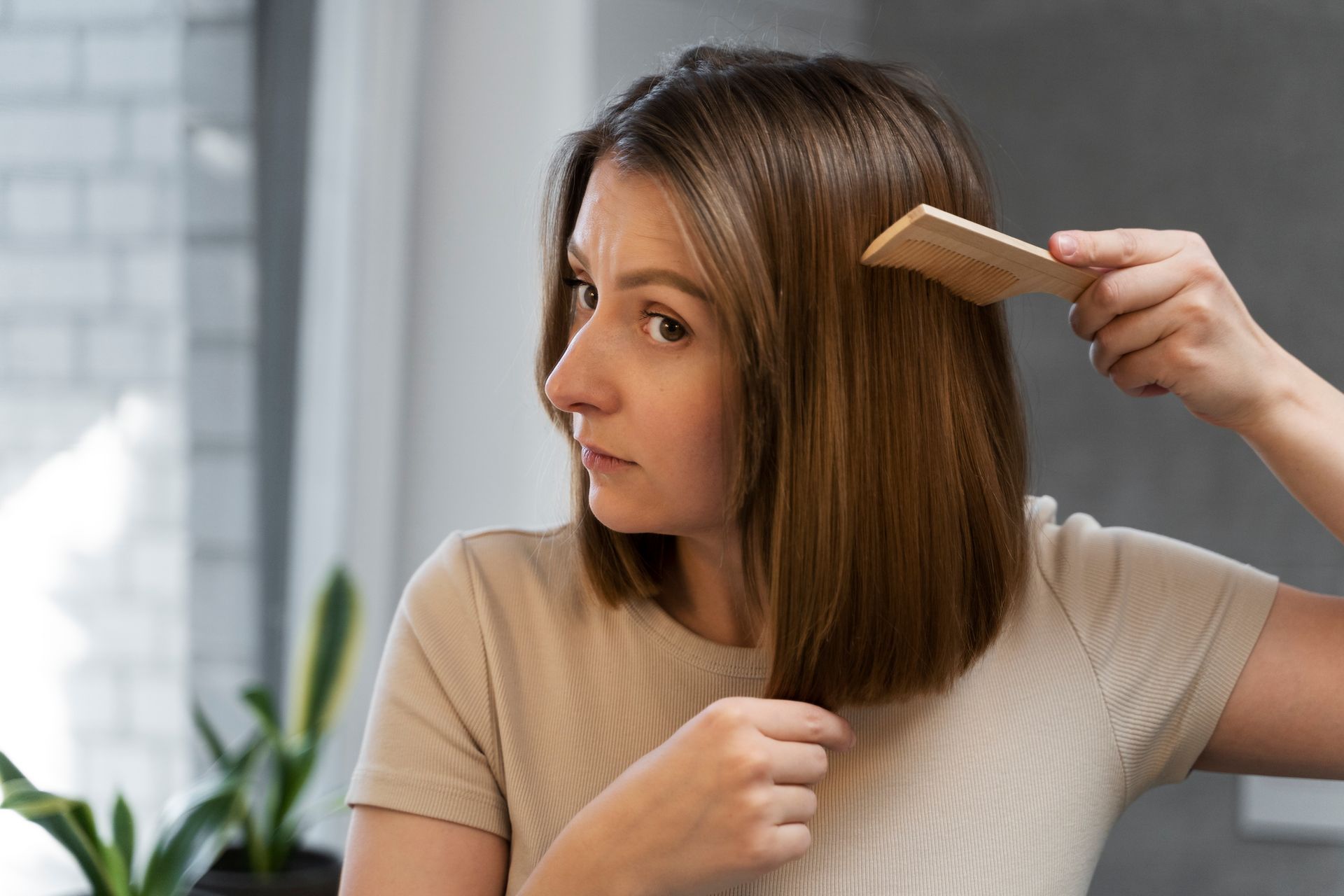 A woman is brushing her hair with a wooden comb.