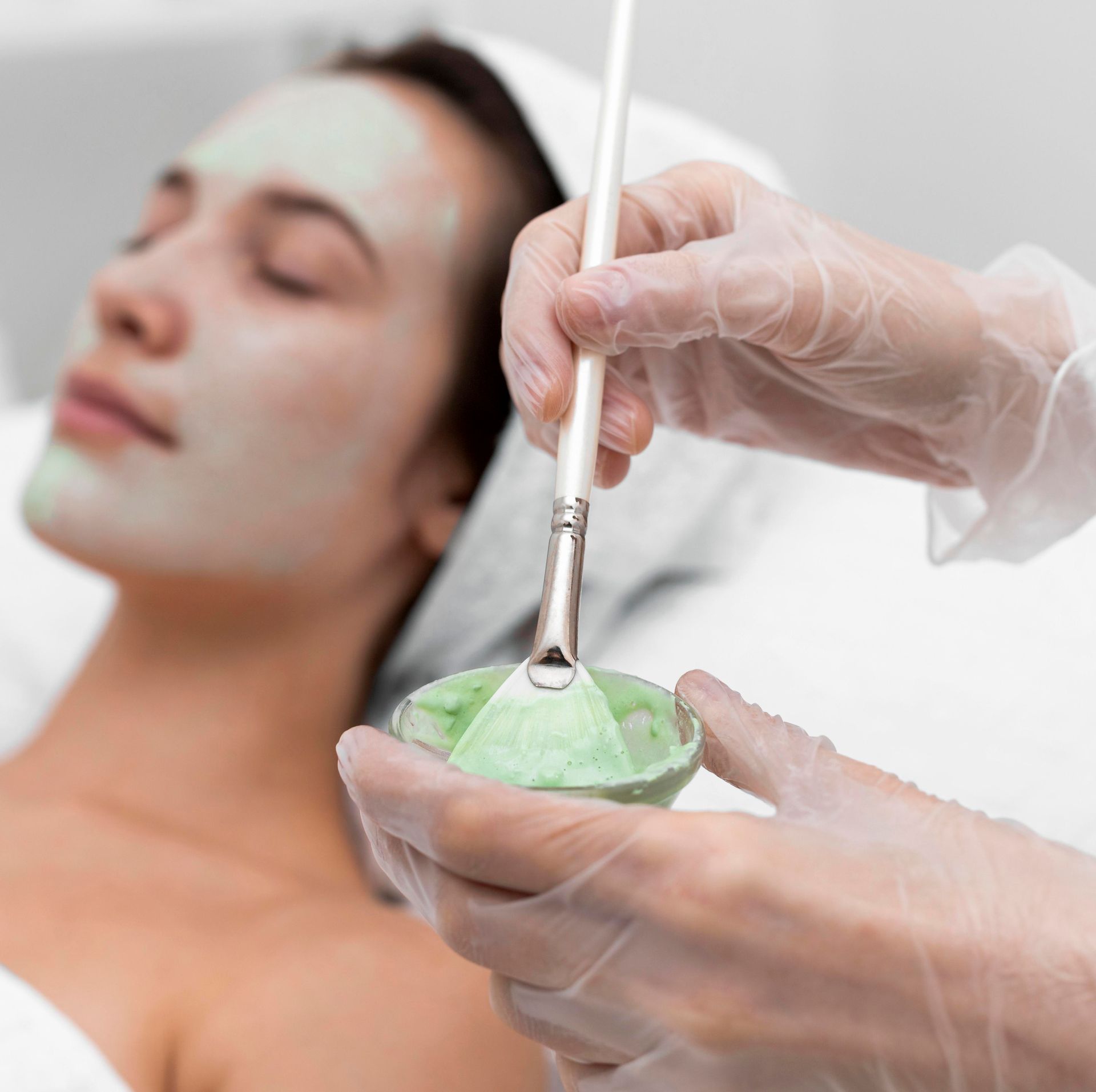 a woman with a green mask on her face is getting a facial treatment .