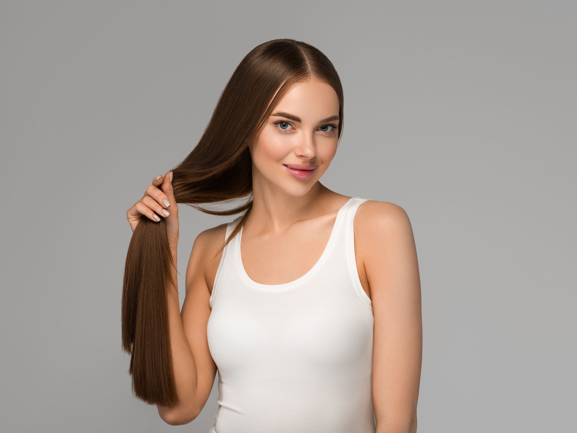 a woman in a white tank top is holding her long hair .