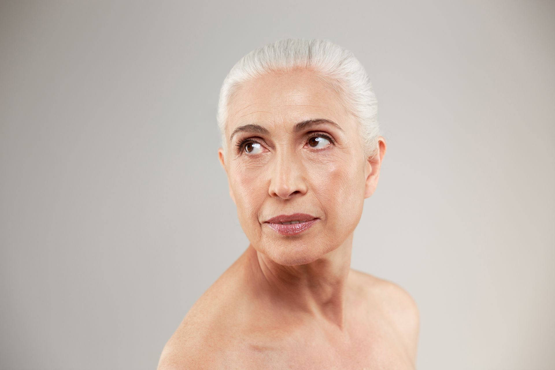 An older woman without a shirt is looking at the camera.