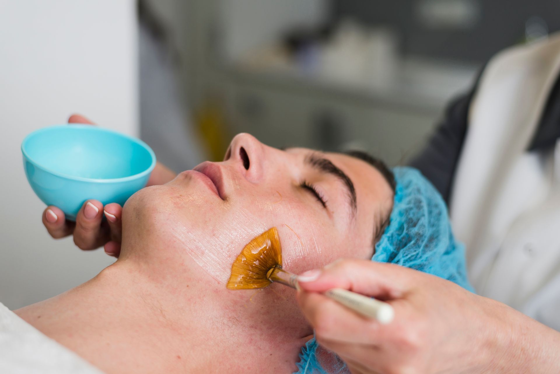 Person receiving a facial treatment; an esthetician applies a mask to the face with a brush.