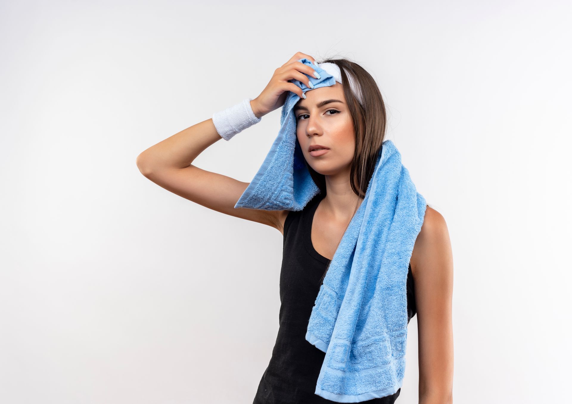 A person in a black tank top and wristband wipes sweat from their forehead with a blue towel against a white background.