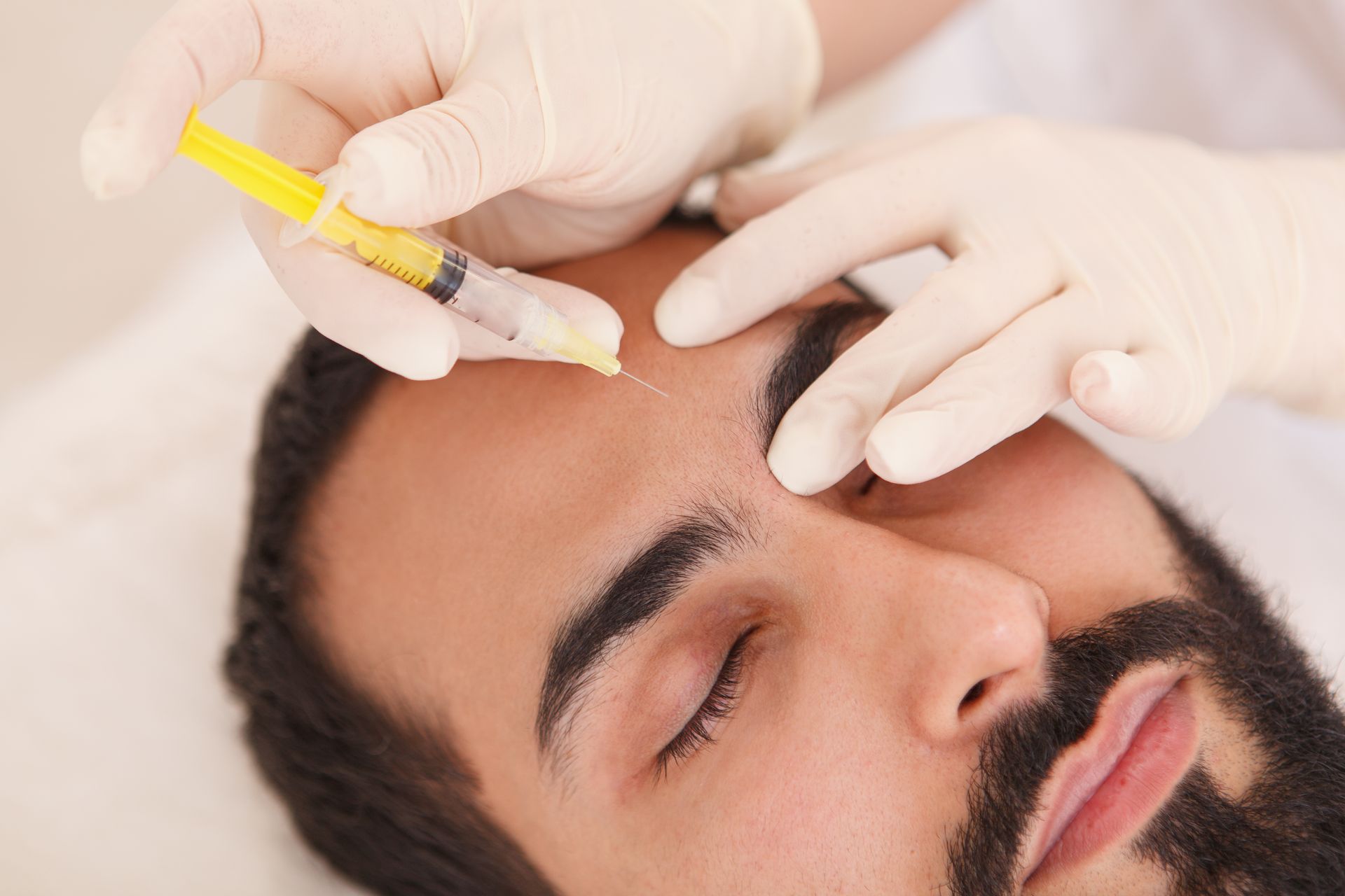 a man with a beard is getting a botox injection in his forehead .