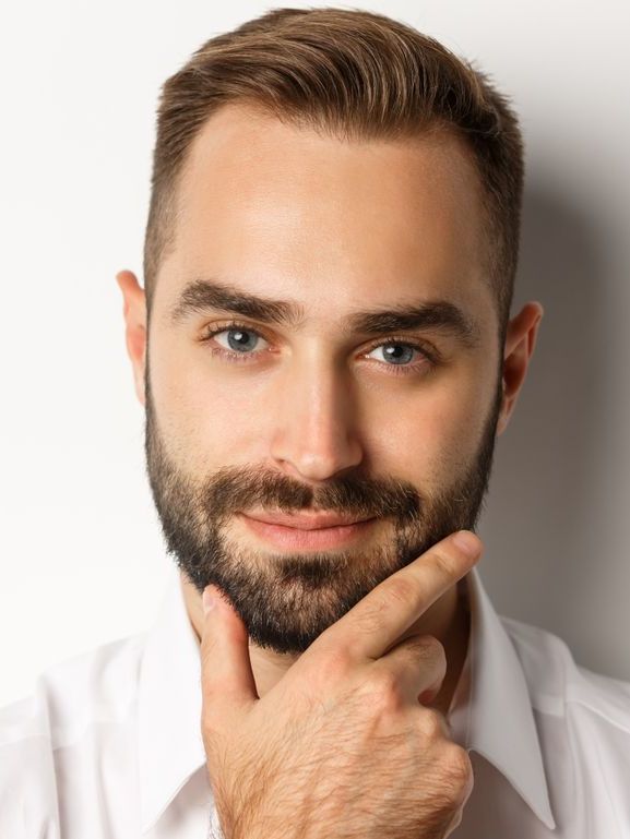 A man with a beard is holding his hand to his chin and smiling.