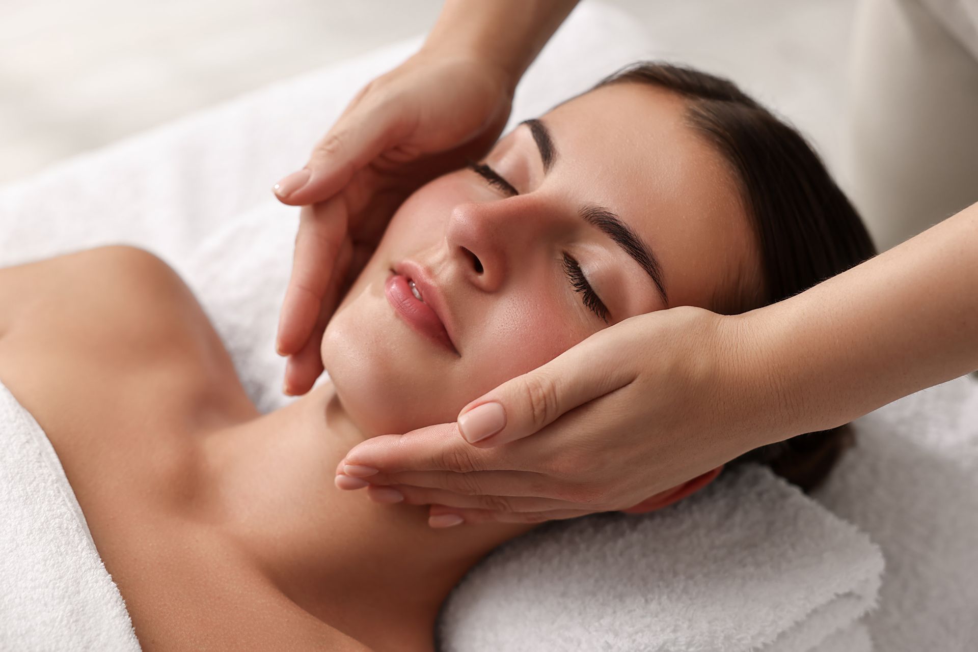 Woman receiving a facial massage on a treatment bed, eyes closed, in a spa setting