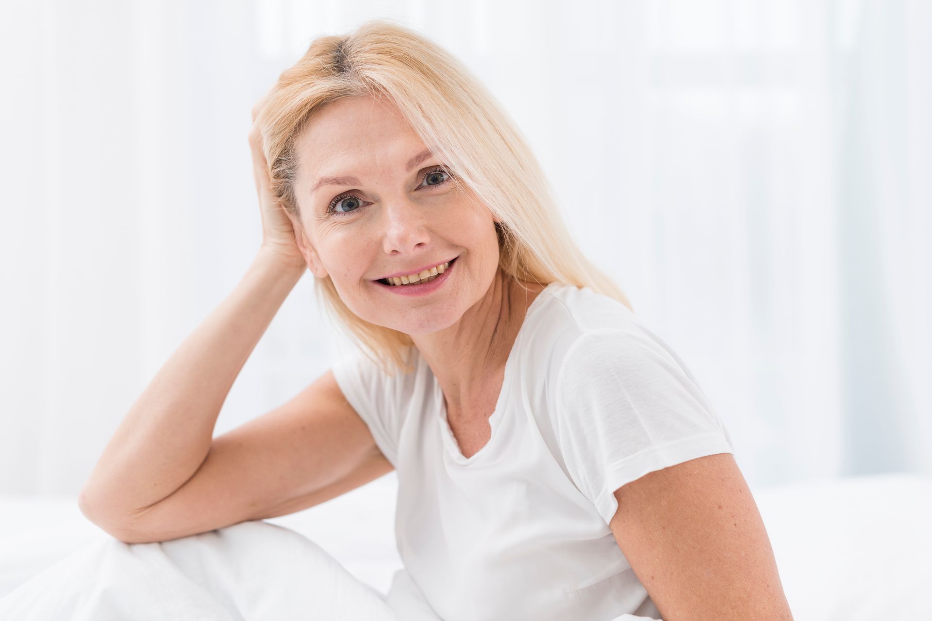a woman in a white shirt is sitting on a bed and smiling .