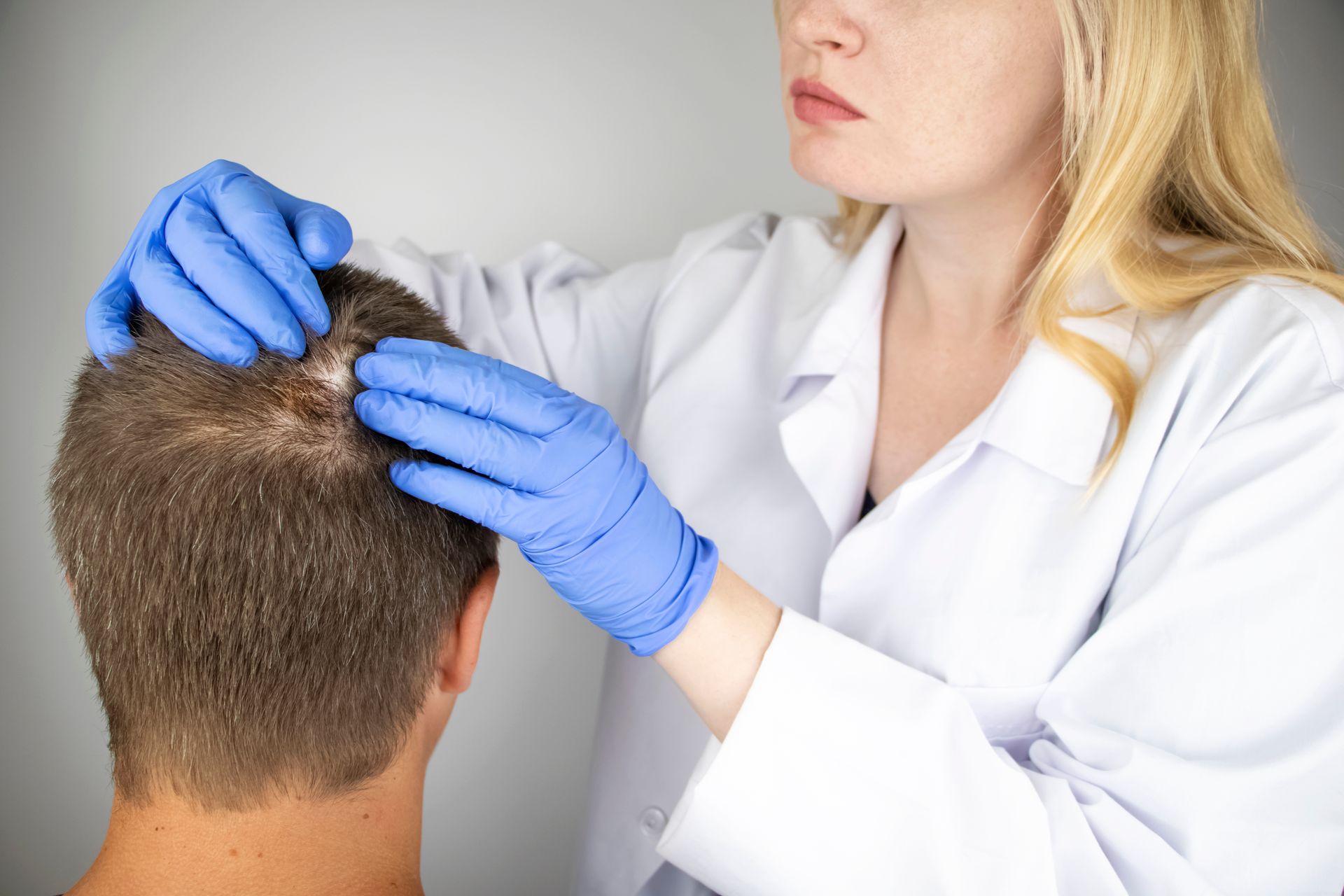 a doctor is examining a man 's hair with blue gloves .
