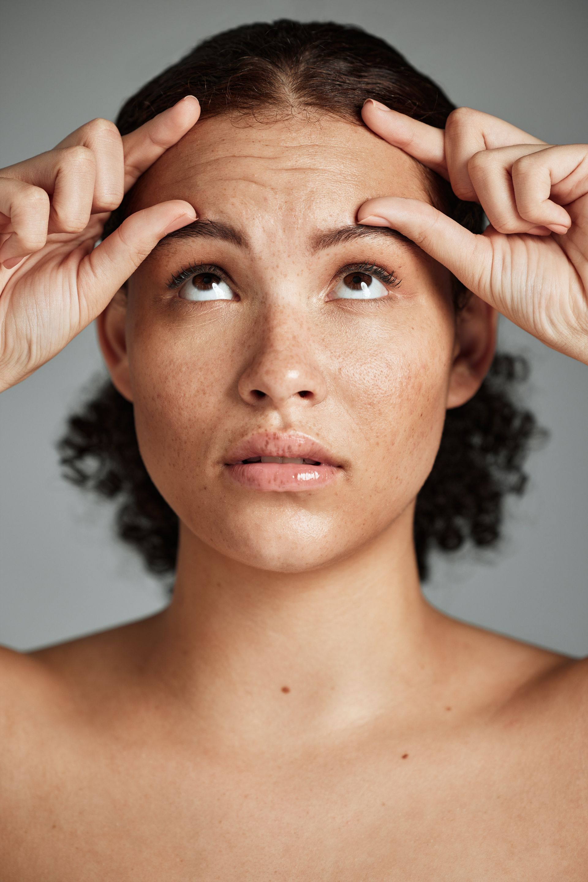 a woman is touching her forehead with her hands and looking up .