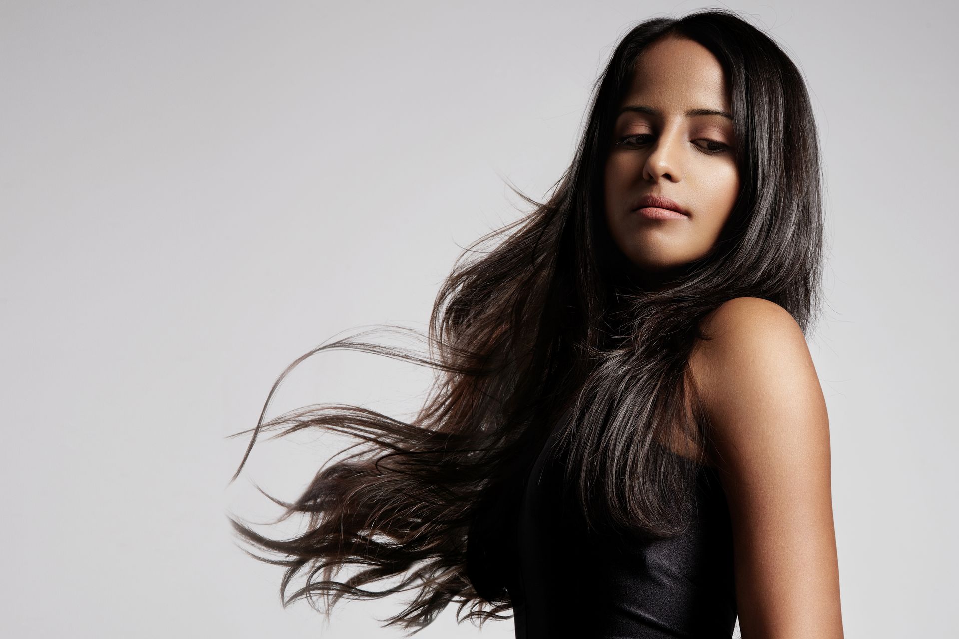 A woman with long hair is wearing a black dress and her hair is blowing in the wind.