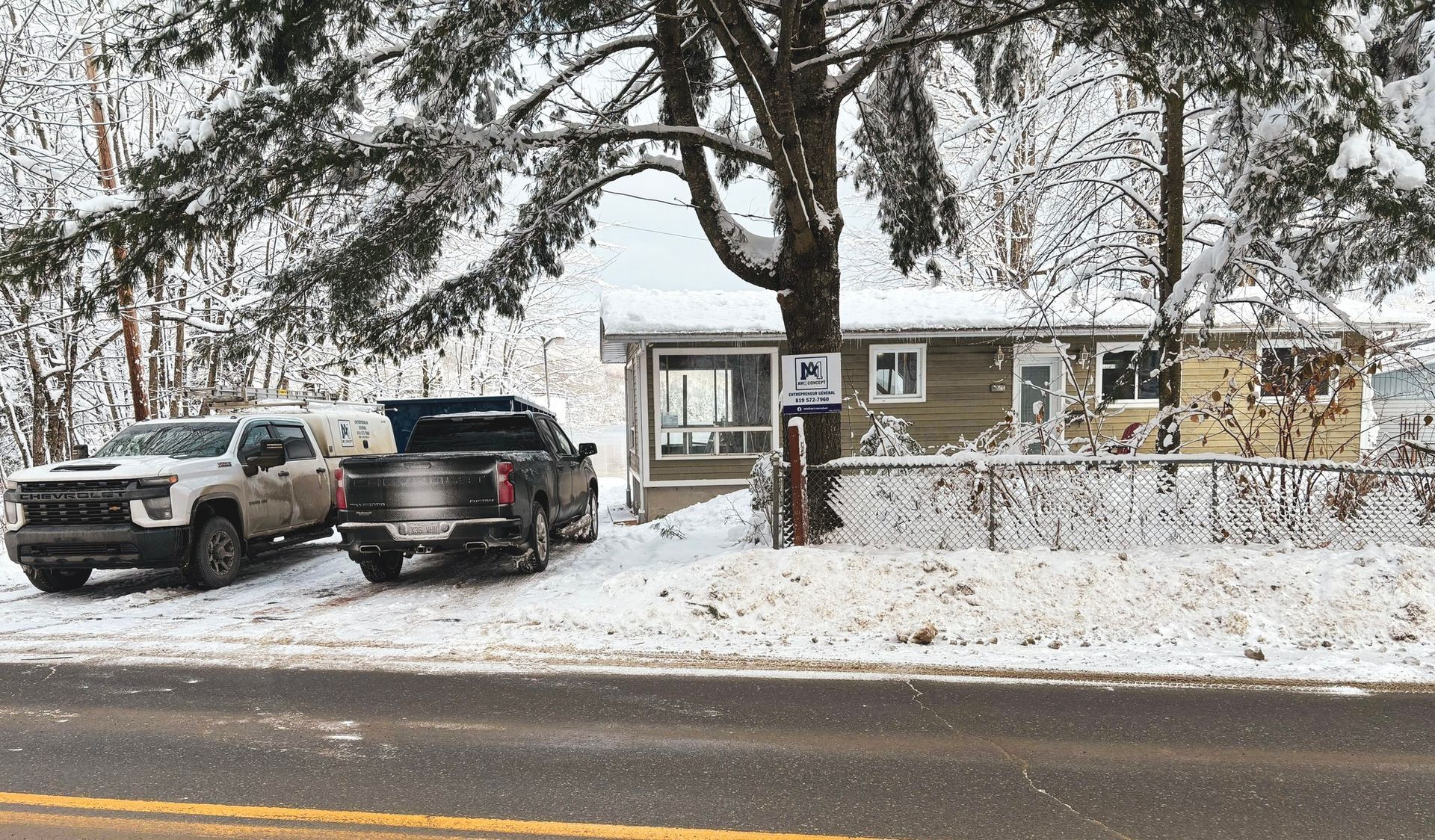 Deux camions sont garés devant une maison recouverte de neige.