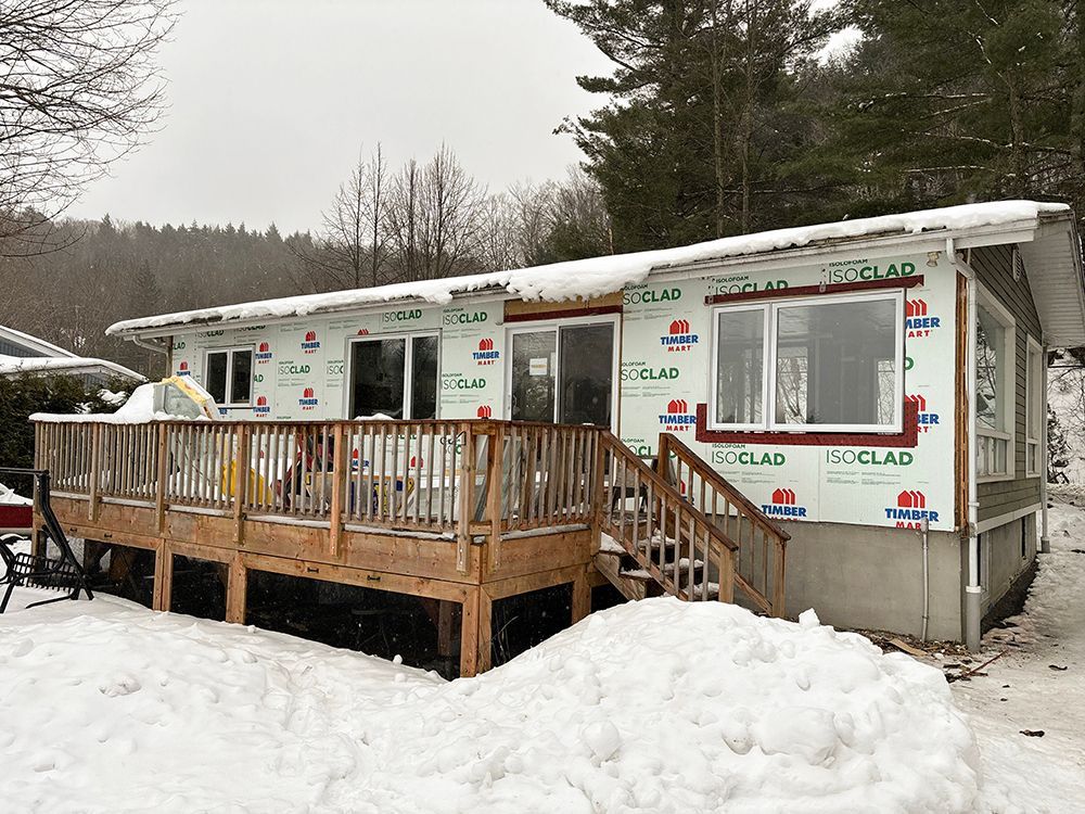 Une maison avec une terrasse et des escaliers est recouverte de neige.