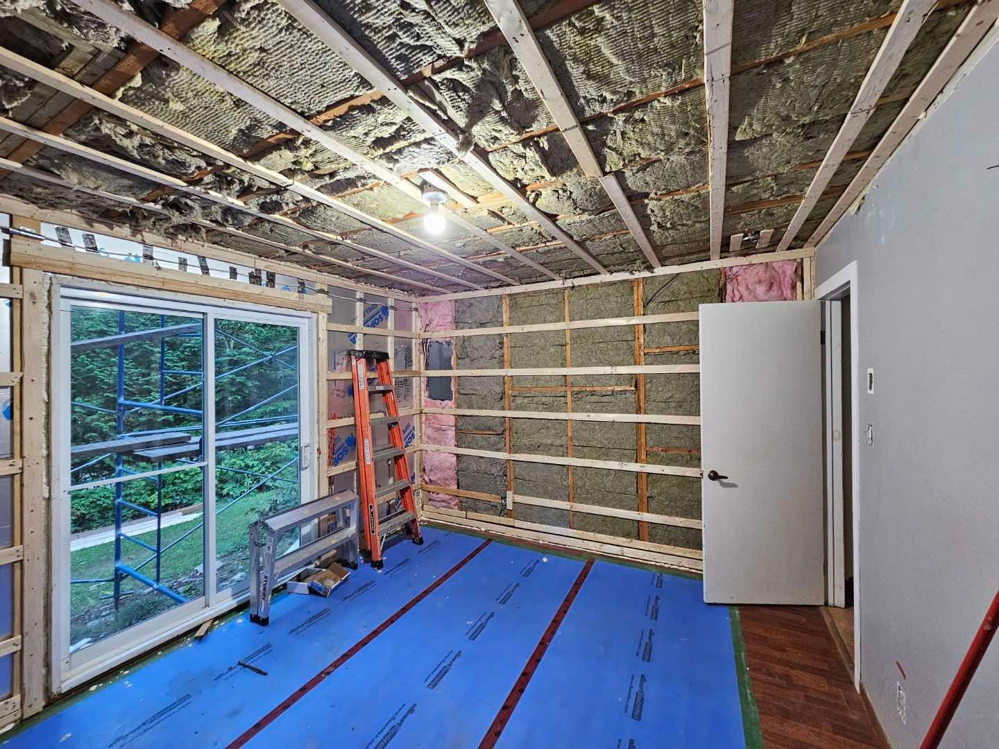 Une pièce avec une échelle et une bâche bleue sur le sol.