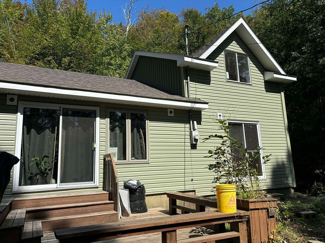 Une petite maison verte avec une terrasse en bois devant.