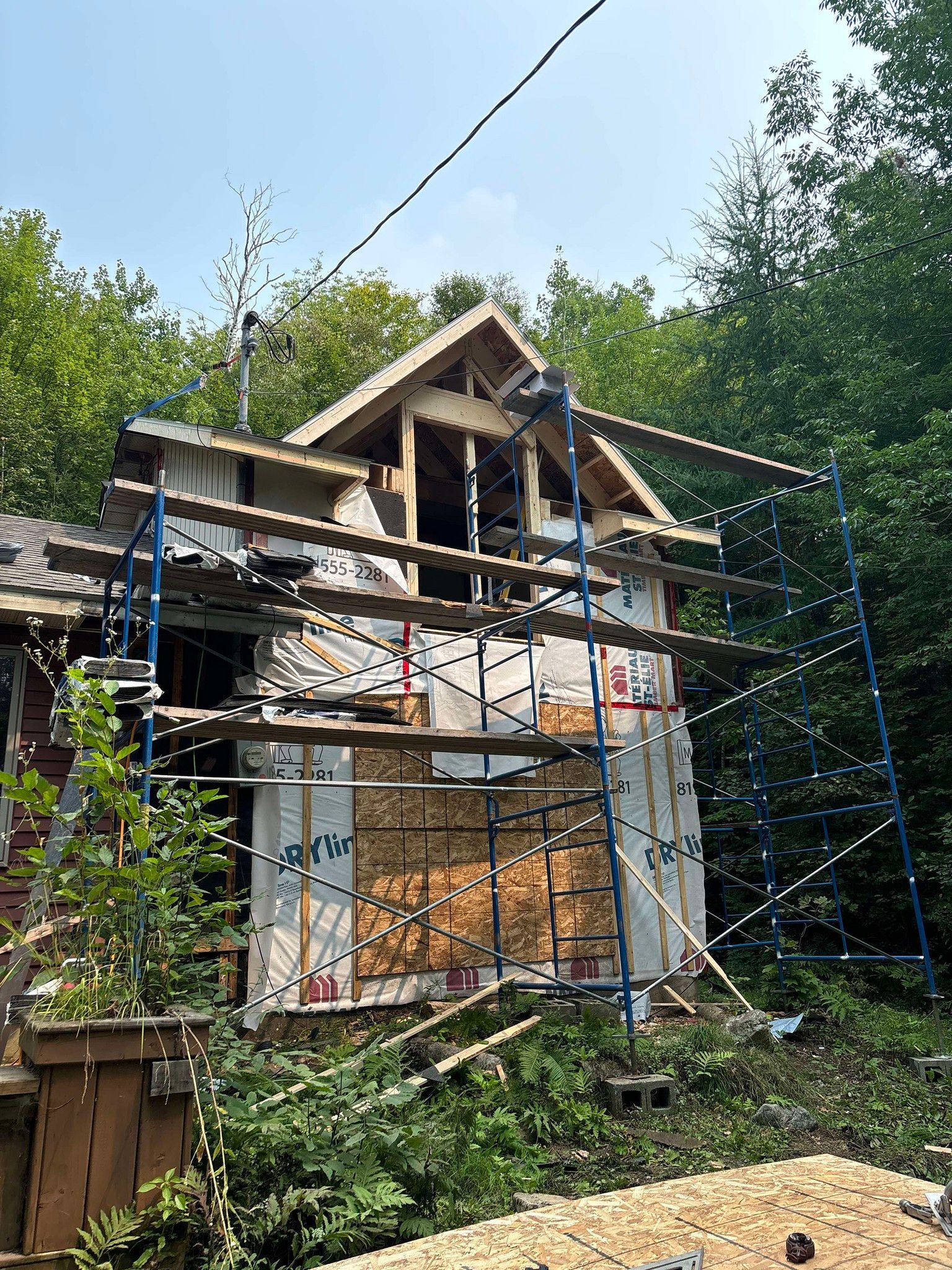 Une maison est en construction dans les bois avec des échafaudages autour.
