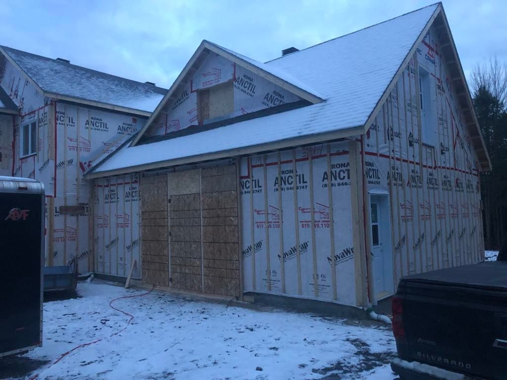Une maison est en construction dans la neige avec un camion garé devant.