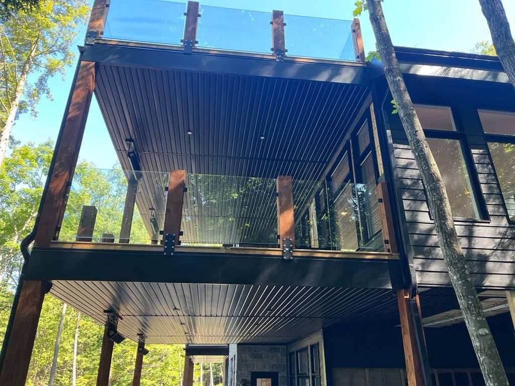 Une maison avec un balcon et une balustrade en verre entourée d'arbres.