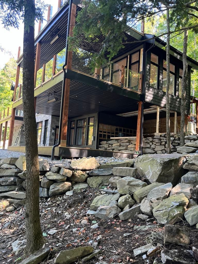 Une grande maison est située au sommet d'une colline rocheuse au milieu d'une forêt.