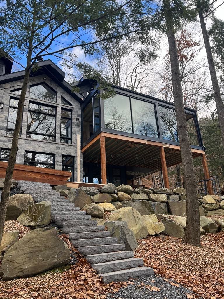 Une grande maison avec beaucoup de fenêtres est entourée d'arbres et de rochers.