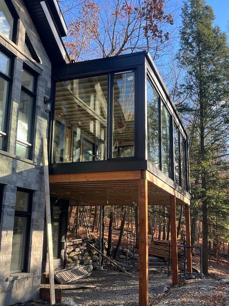 Une maison avec une grande terrasse et beaucoup de fenêtres entourée d'arbres.