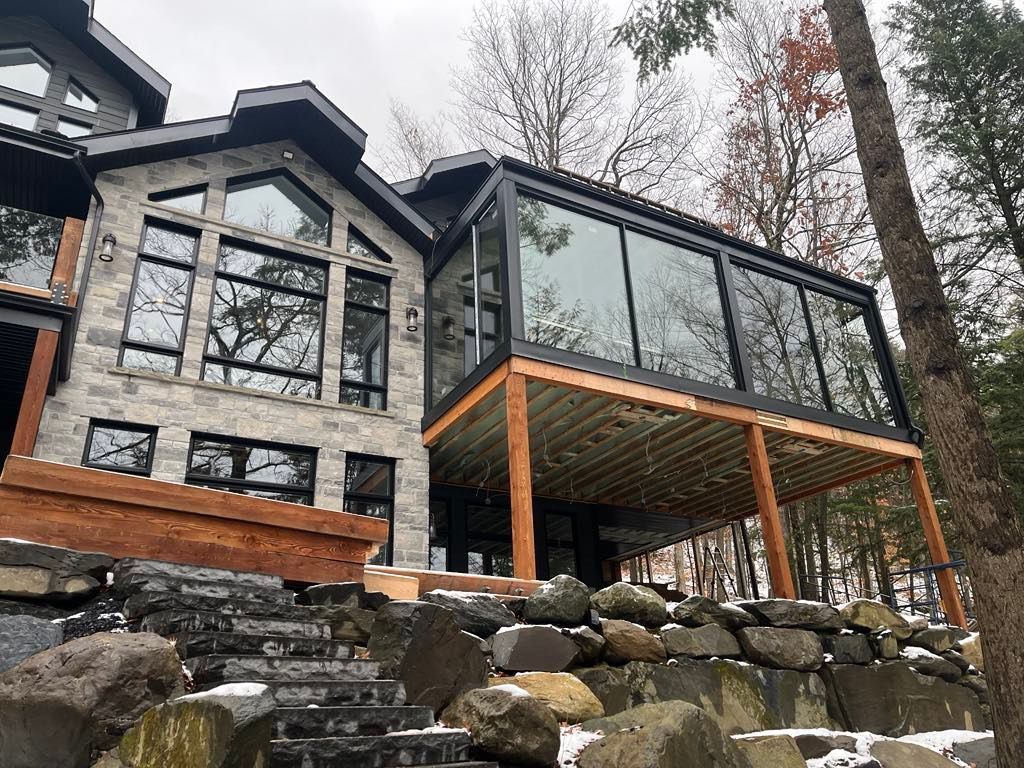 Une grande maison avec beaucoup de fenêtres et une grande terrasse entourée d'arbres.