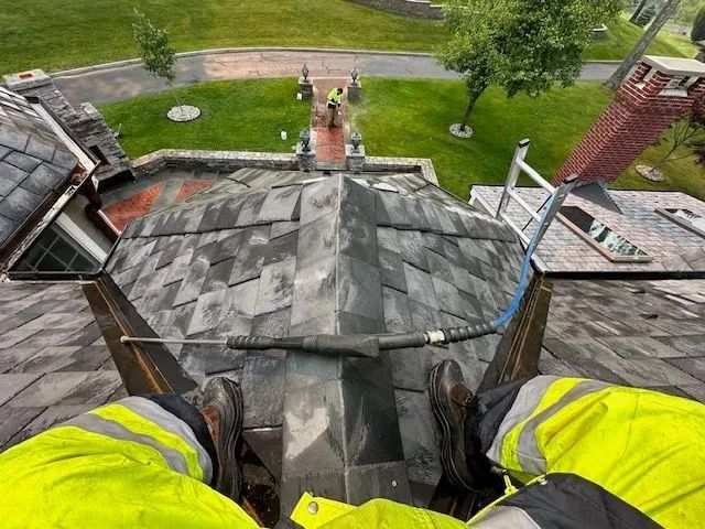 View from a roof, worker in safety vest and boots, cleaning slate tiles.