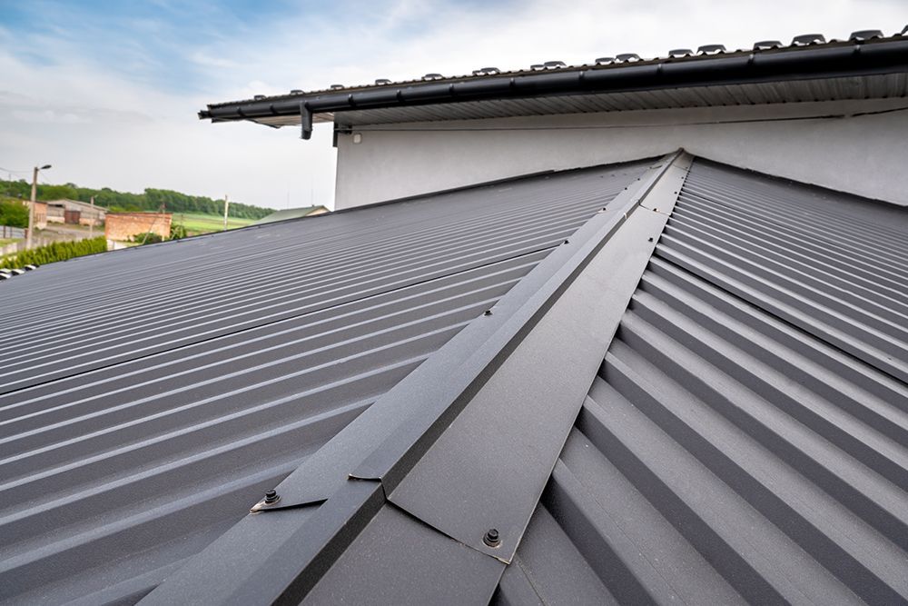 Gray metal roof with ridge cap; close-up view on a sunny day.
