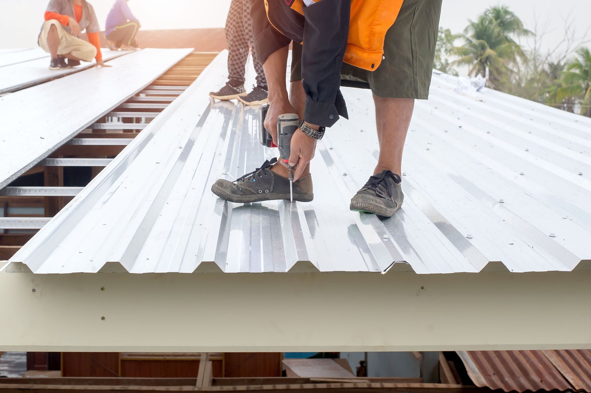 Workers installing white corrugated metal roofing panels on an outdoor building frame.
