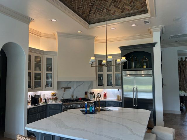 Elegant white kitchen with marble island, stainless fridge, and ornate ceiling details