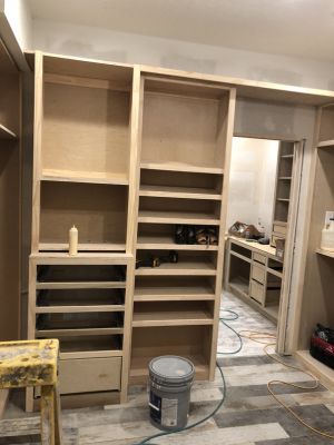 Unfinished wooden built-in cabinets and shelves in a room under renovation, with tools and a paint bucket on the floor.