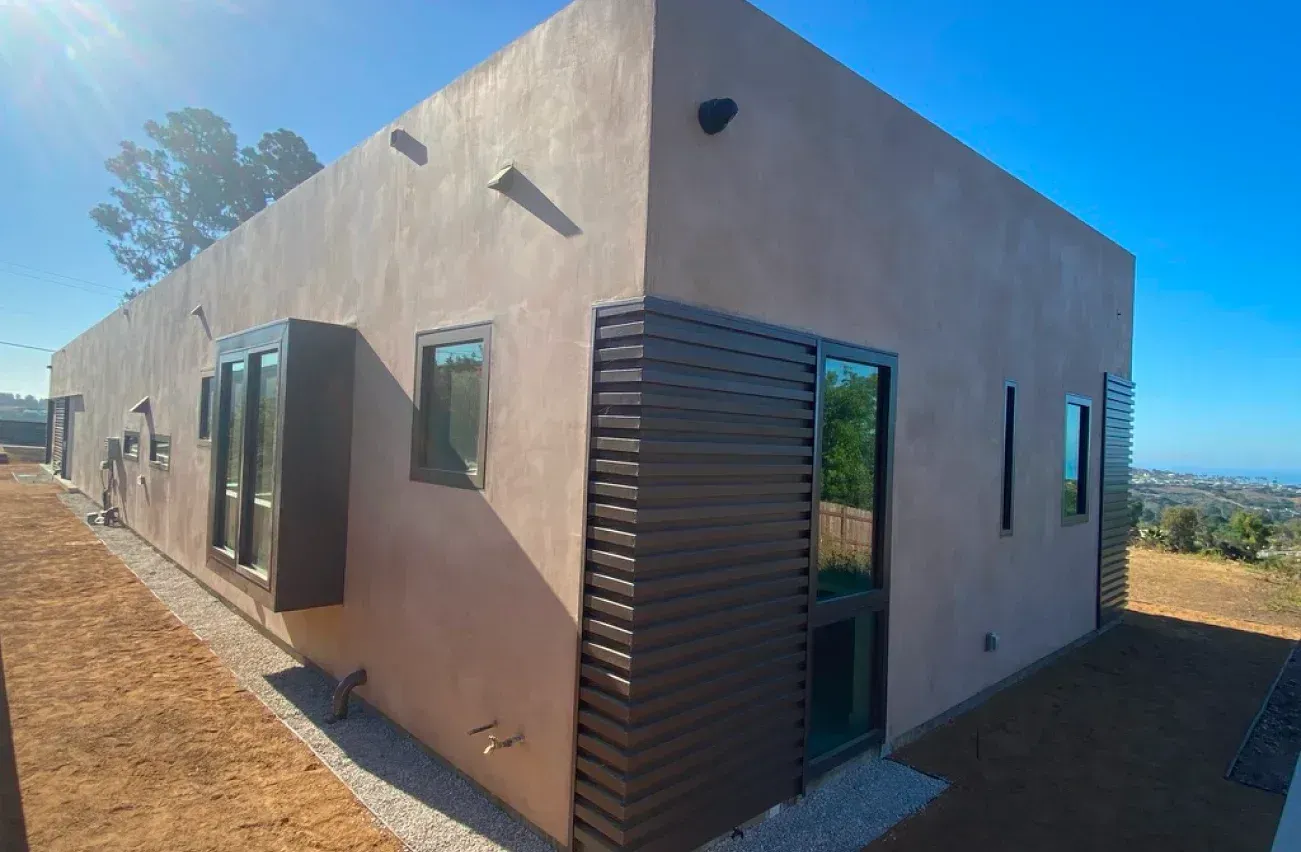 A house with a lot of windows is sitting on top of a dirt hill.
