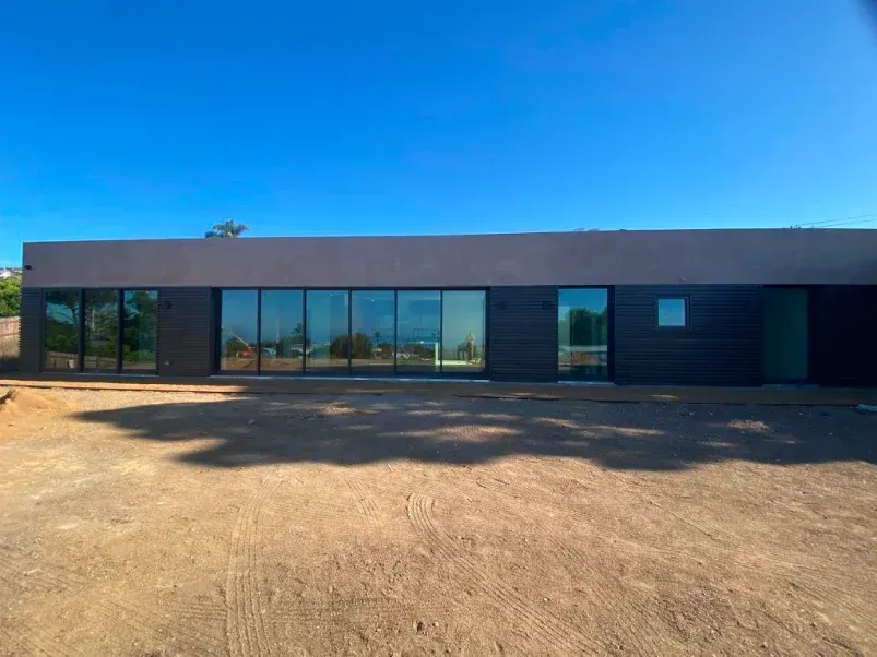 Modern, dark-colored house with large glass windows under a clear blue sky.