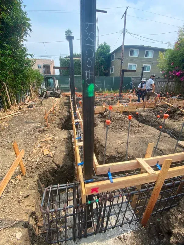 Construction site with steel beams, concrete forms, rebar, and workers.