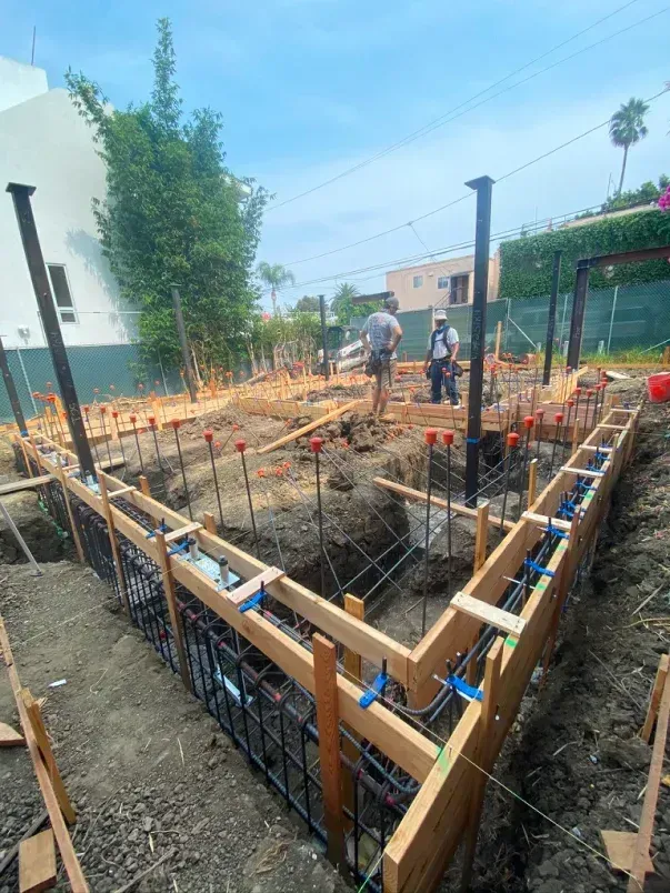 Construction site with wooden frames and rebar, workers, and a partially excavated foundation.