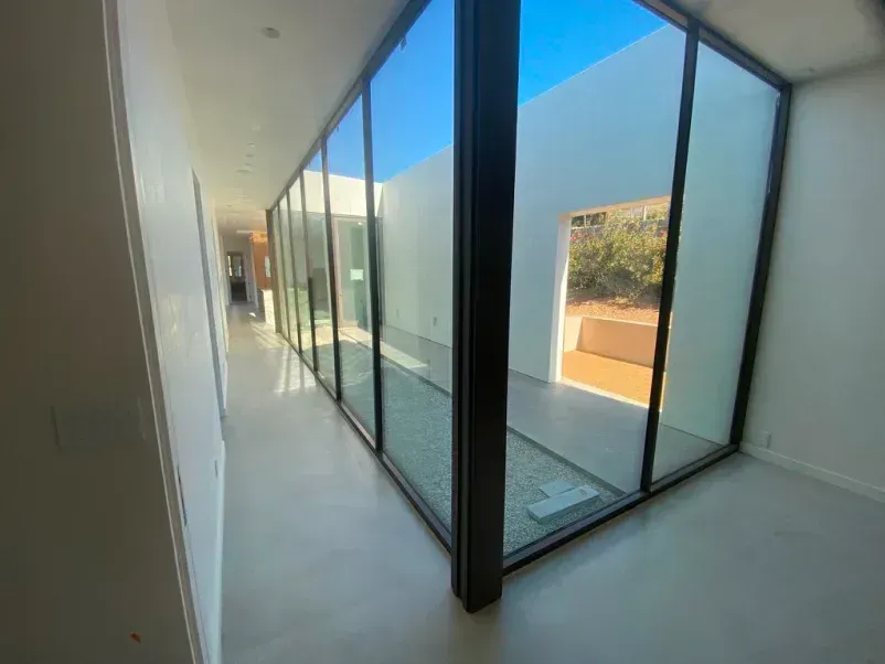 Hallway with large glass windows facing a courtyard with light gray floor and white walls.
