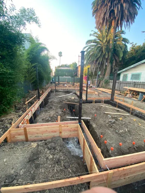 Construction site with wooden forms for foundation in a yard, dirt, palm trees.