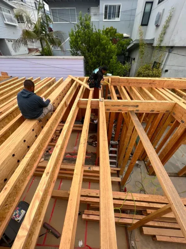 Construction workers on wooden roof frame; two men building, sunny day.