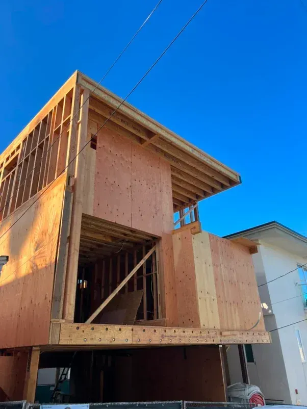 Two-story wooden building under construction against a clear blue sky.