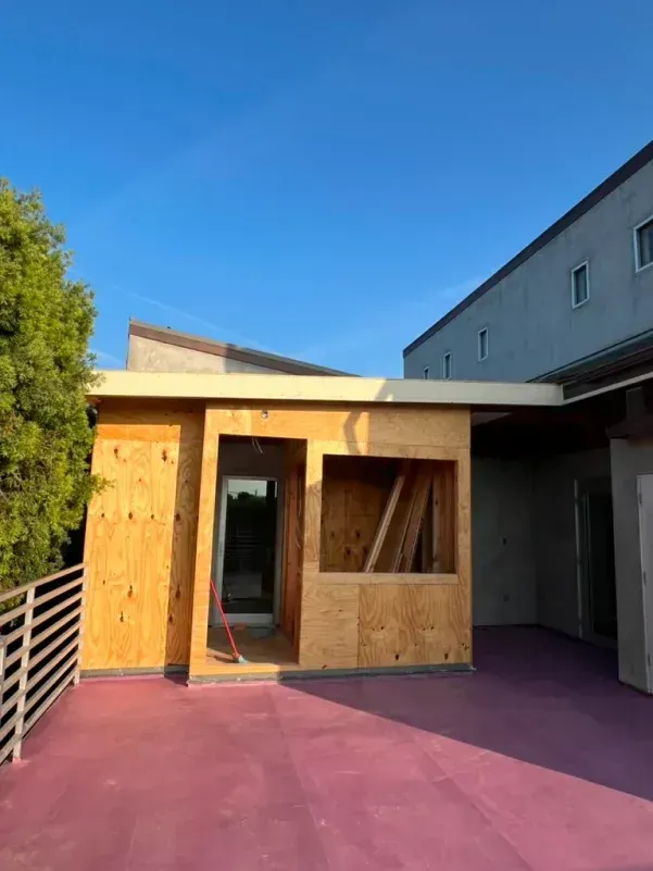 Construction of a wooden structure on a rooftop patio with pink surface and blue sky.