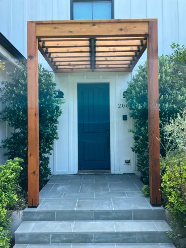 Wooden pergola over a teal door with steps leading up.