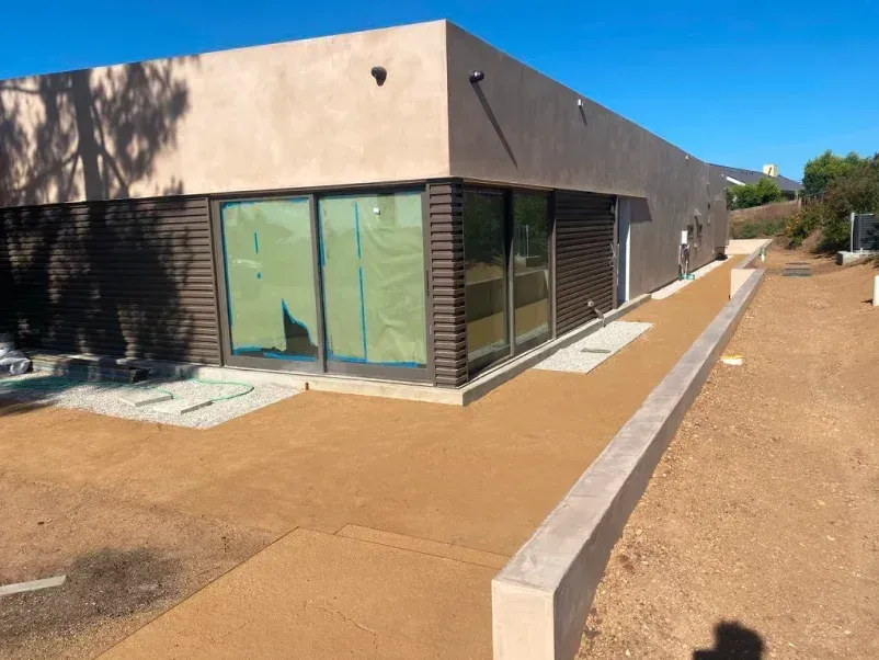 Tan building with glass windows, brown siding, and a concrete walkway on a sunny day.