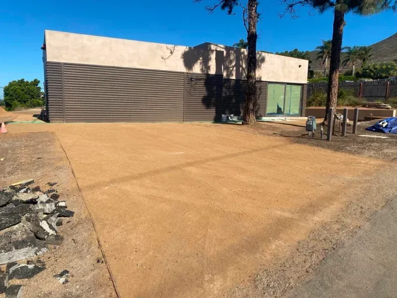 Sandy parking area in front of a modern building with brown slats and a glass door on a sunny day.